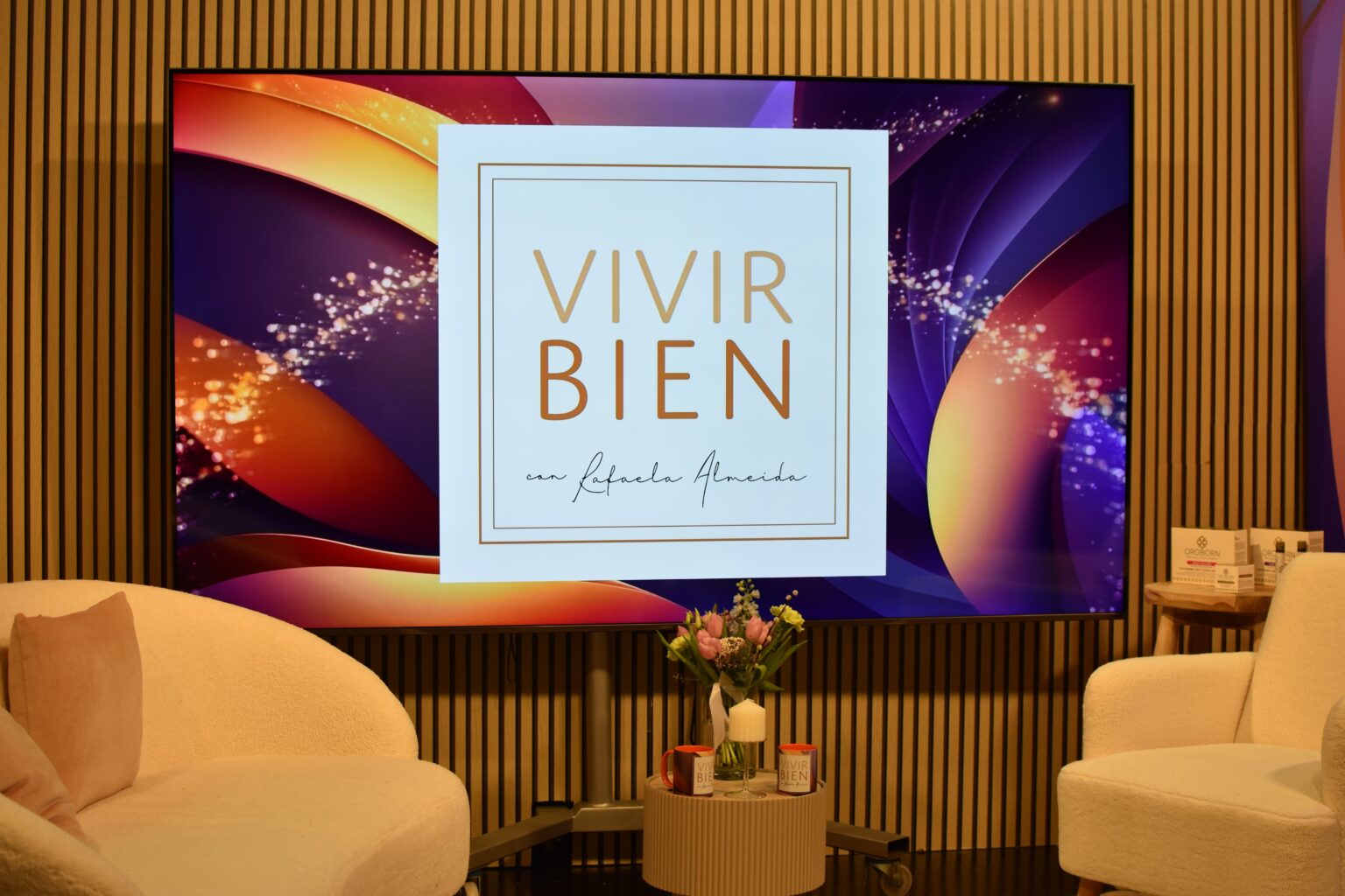 Plató de Vivir Bien con Rafaela Almeida: butacas, mesa auxiliar y el logotipo del programa en la pared del decorado